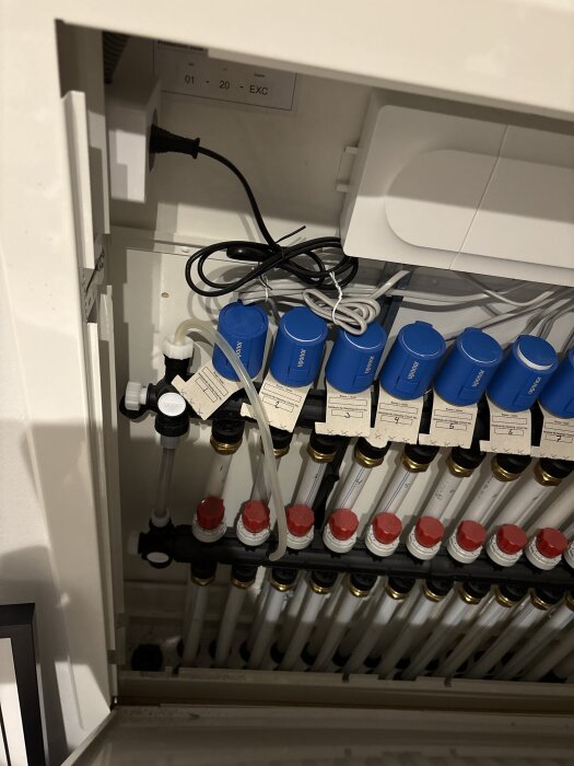Golvvärmesystem med vita och röda ventiler samt blåa motorer, slang ansluten för avluftning av systemet.