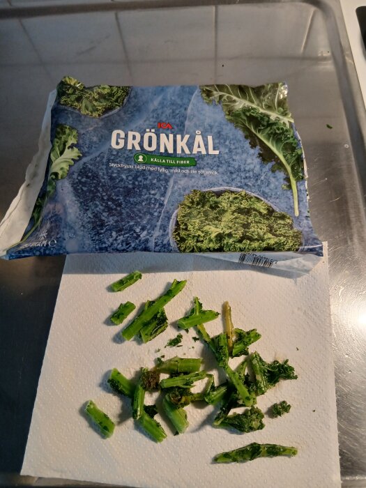 Paket med ICAs frysta grönkÄl och urplockade grönkÄlsstjÀlkar pÄ papper.