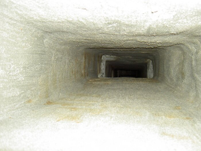 Rektangulär kanal i betong med sliten yta, som liknar ett ventilationsschakt eller skorsten, sedd i perspektiv mot djupet.
