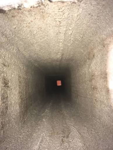 Rakt skott inuti ett murat eller betongbelagt ventilationsschakt, med svagt ljus vid bortre änden.