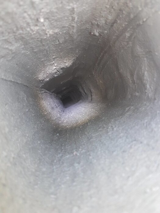 Insidan av en smal, mörk kammare eller ett rör med ojämna väggar som sträcker sig bortåt i mörker, fotograferat i vertikal vy.