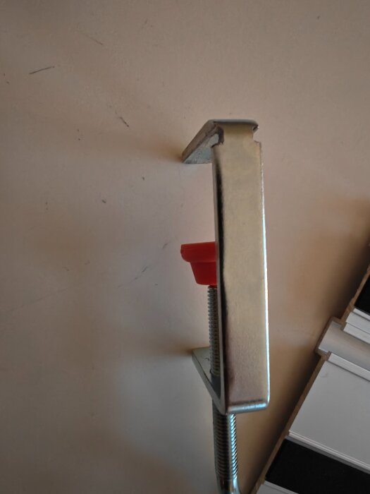 Metalltving med röd detalj, fäst på vit yta, användbar vid sågning och renoveringsprojekt.