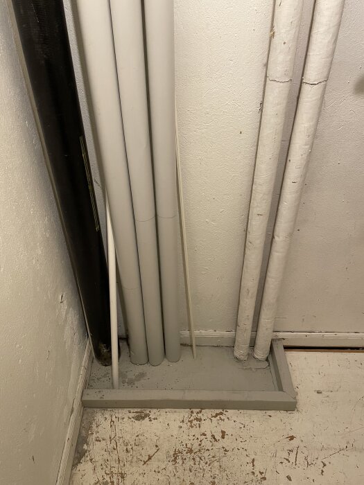 Rör och regel i ett hörn av en klädkammare, där en vägg planeras att byggas för att dölja installationen.