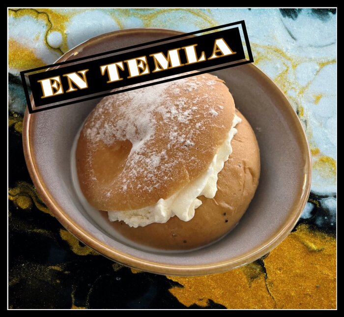 Bulle med grädde, även kallad semla, på en tallrik. Texten "En temla" finns ovanför bullen.