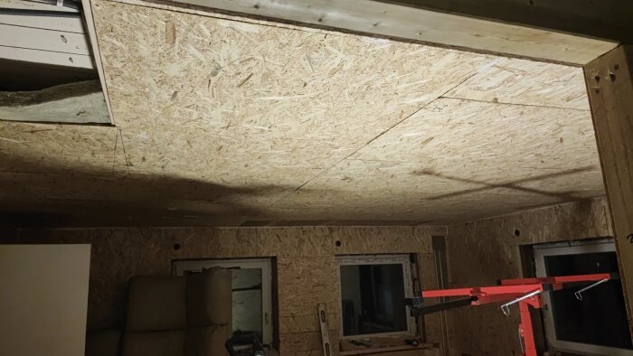 OSB-skiva installerad i ett nästan färdigt innertakprojekt med synliga fönsteröppningar och byggmaterial i bakgrunden.