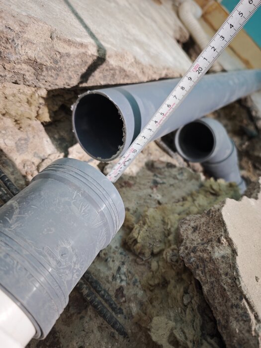 Måttband visar diametern på ett grått avloppsrör i betongmiljö med isolering.