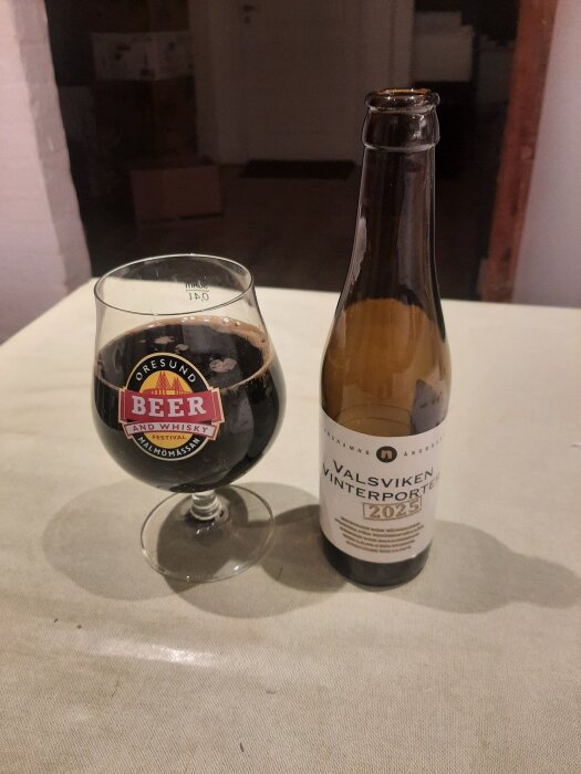 Ett glas med mörk porter och en flaska Valsviken Vinterporter 2023 på ett bord.