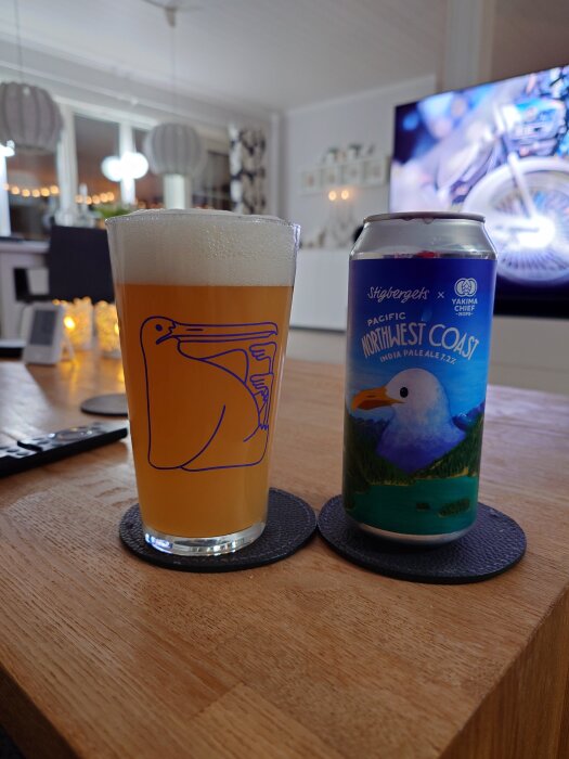 Ölglas med Stigbergets Pacific Northwest Coast IPA bredvid en burk, på ett bord i ett modernt vardagsrum.