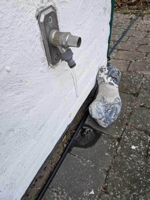 Utkastare på utsida av byggnad med istapp hängande från pipen, intill en sten på marken.