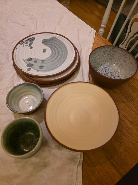 Flera keramikskålar och tallrikar med olika mönster och färger placerade på en dukad yta.