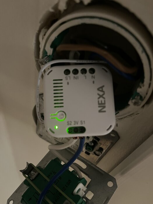 Nexa-styrmodul installerad med kopplade kablar, inuti en apparatlåda iscensatt med grönt lysande indikator.