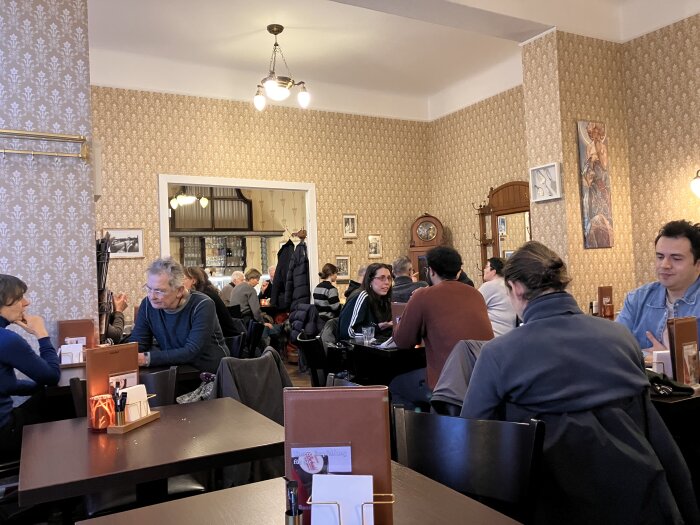 Caféinteriör på Buchwald, Bartningalle 29, Berlin, med gäster som sitter vid bord i ett klassiskt inrett rum med mönstrade tapeter.