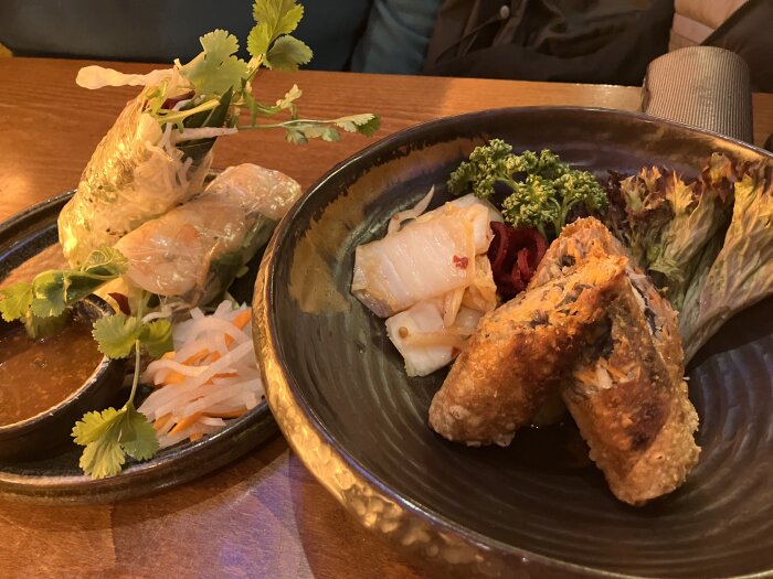Assorted spring rolls and duck served with garnish and dipping sauce.