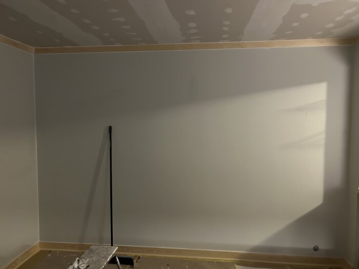 Vägg och tak under renovering med synliga skarvar i taket, ett verktyg lutat mot en enkel stege eller pall på golvet.