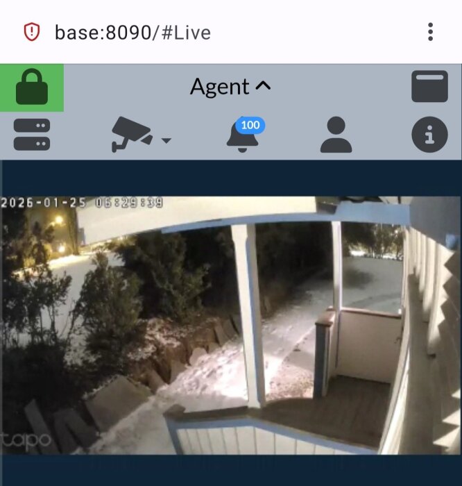 Övervakningskamera visar en snötäckt veranda och trädgård i nattljus, ses via programmet Agent DVR på en dator.
