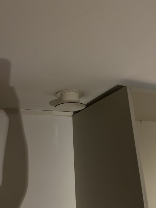 Tilluftsventil i taket vid sidan av garderob, skugga från handen syns på väggen.
