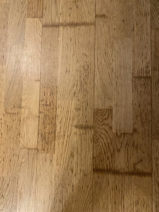 Ljusa parkettgolv med mörkare skarvar mellan brädorna, diskuterad renovering om slipning kan förbättra utseendet.
