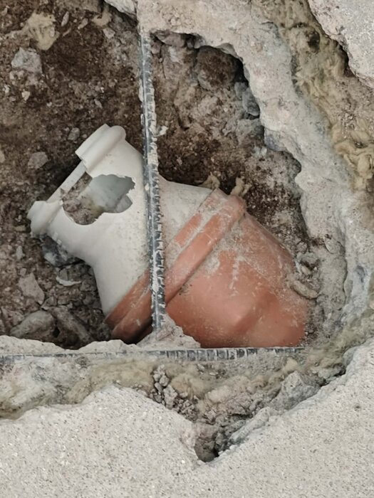 Trasig orange och vit rördel nergrävd i betong, omgiven av grus och cement.