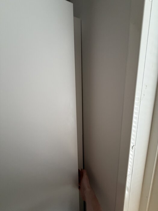 Närbild av en dörr bredvid en täcklist, med en hand synlig på dörren i en smal springa.