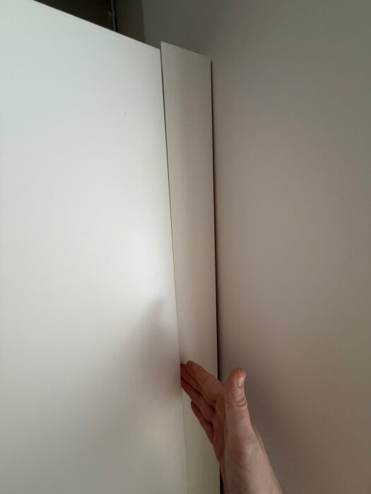 En hand mäter avståndet mellan en dörr och en vägglist för att visa hur nära de ligger.