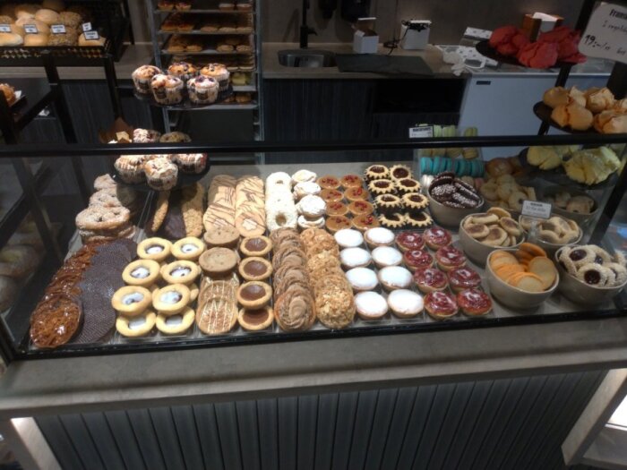 Olika sorters bakverk, inklusive muffins, kakor och tårtor, visas snyggt upp i en glasmonter på ett kafé.