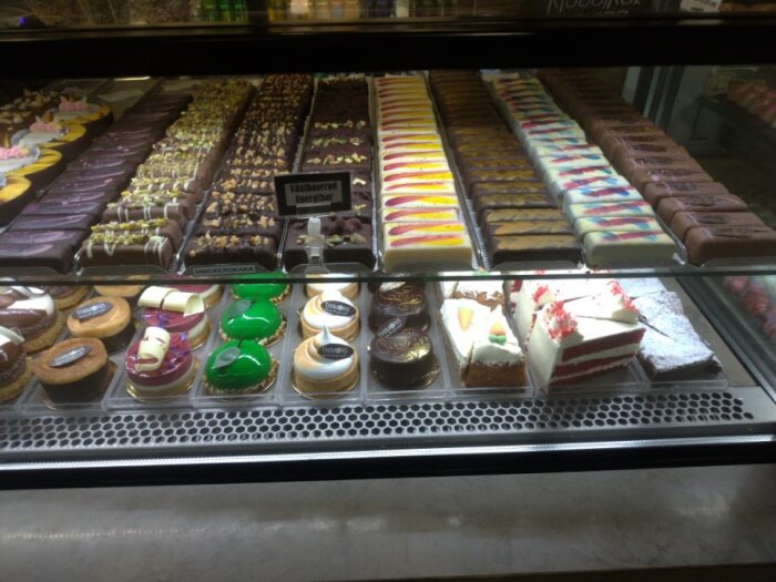Ett kafédisk med olika bakverk, inklusive tårtbitar, chokladkakor och färgglada småkakor, serveras på ett kafé.