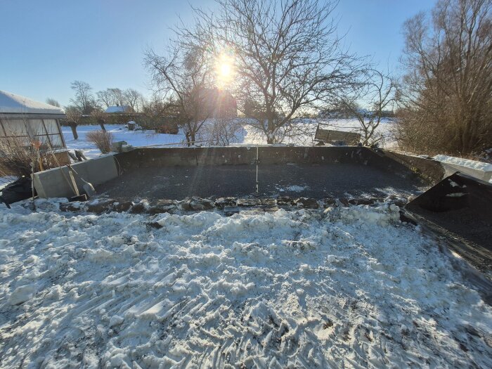 Vinterlandskap med snö och ett påbörjat växthusprojekt med betonggrund, verktyg och kullerstenar i södra Skåne.