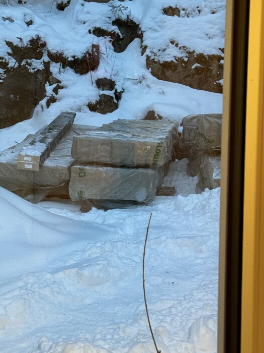Staplar av isoleringsmaterial täckta i plast ligger på en snötäckt mark.