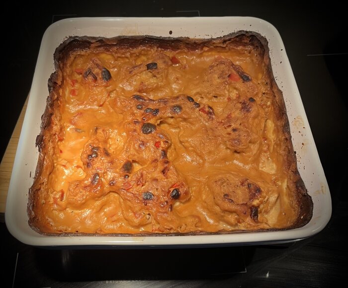 Ugnsform med Sweet Jelena Chicken, synliga brända kanter och krämig sås, färdiglagad men något överstekt.