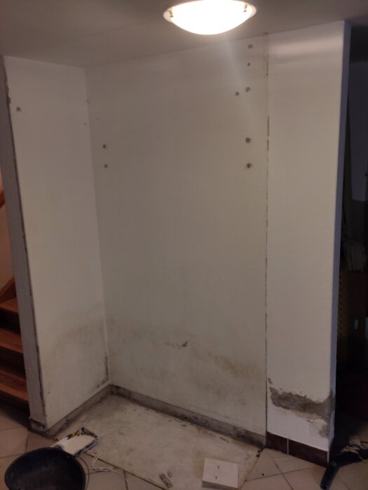 Tomt hörn med vita väggar och avskalat golv där en garderob tidigare stod, omgiven av mörka skrapmärken och lämpat för renovering.