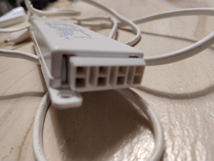 Närbild av en vit transformator med flera anslutningsuttag och elkablar, placerad på en ljus bordsyta.