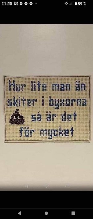 Väggbonad med texten "Hur lite man än skiter i byxorna så är det för mycket" och en broderad bajs-emoji.
