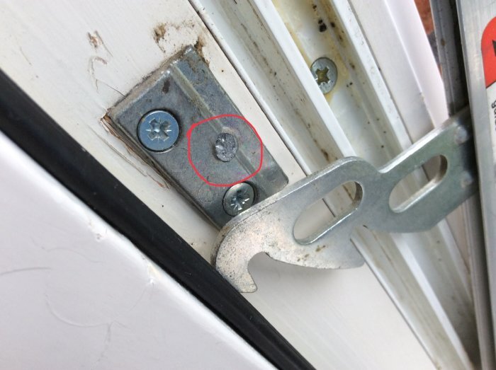 Fönsterbeslag med markering runt en skruv, möjligvis för att påvisa ett problem med fönsterfästet eller mekanismen.