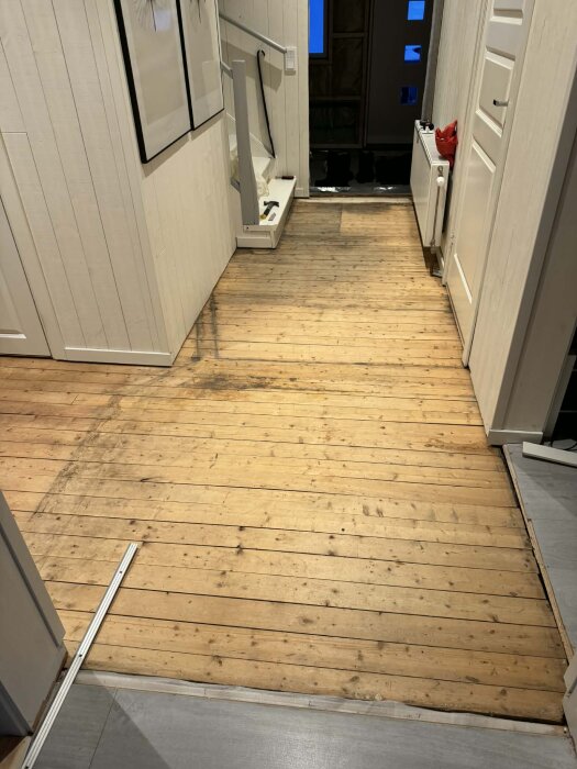 Gammalt trägolv i en hall under renovering; planen är att lägga golvvärme, glespanel och övergolv för att åtgärda ojämnheter och knarr.