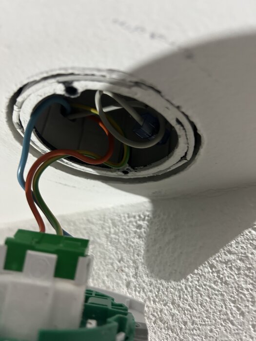 Elektrisk dosa i tak med synliga kablar och ett Schneider-uttag, montageproblem på grund av metallklor som är i vägen.