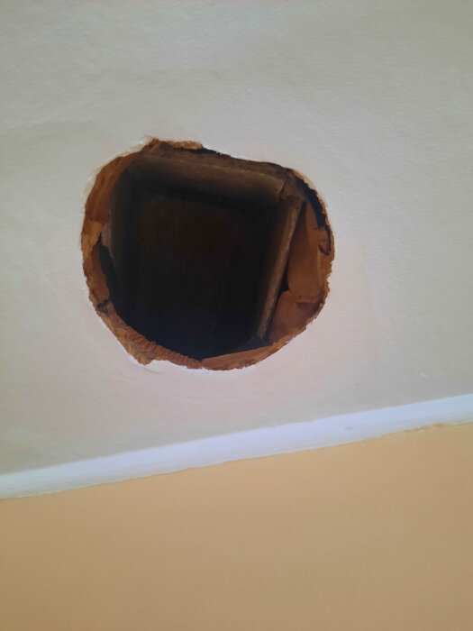 Rund öppning i tak med fyrkantig ventilationskanal synlig, omgiven av vit och beige yta.