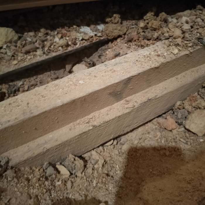 Närbild av reglar vilande på betong med utfyllnad av slaggsten mellan dem, del av golvkonstruktion för planerad golvvärmeinstallation.