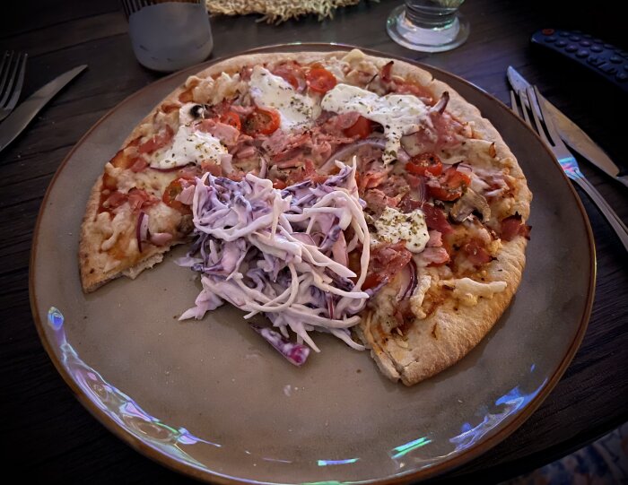 Pizza med skinka, svamp, tomater och ost, serverad med coleslaw på en tallrik.