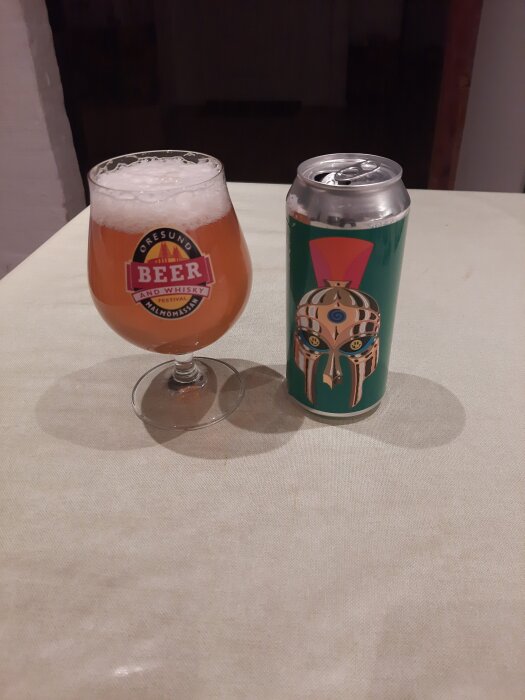 Ett glas öl med skum från Øresund Beer and Whisky Festival och en burk med dekorativt mönster står på ett bord.