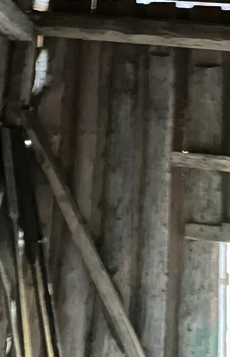 Gamla träbjälkar i en byggstruktur med spadar lutade mot väggen.