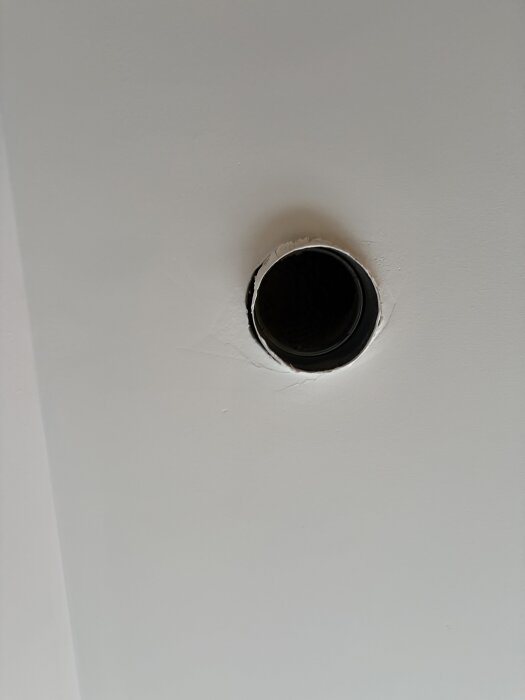 Rund öppning i tak där rör för FTX-system syns, omgiven av nymålad yta.