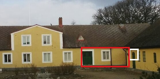 Exteriör av ett äldre hus med gul fasad, flera fönster och en dörr. Taket är av eternit och fasaden lutar något vid fönstret efter dörren.