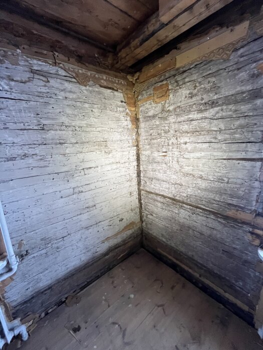 Gammal trävägg i ett torp med möjliga tecken på fuktskador eller mögel längs hörn och kanter.