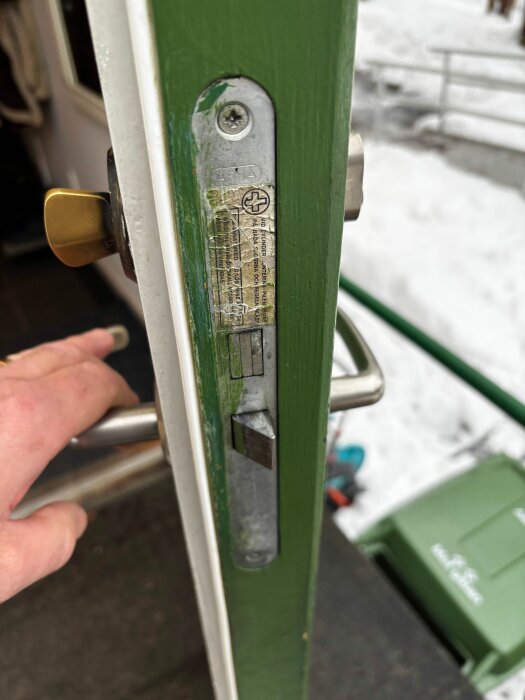 Närbild av ett gammalt dörrlås i en grönmålad dörr med en hand som håller i handtaget.