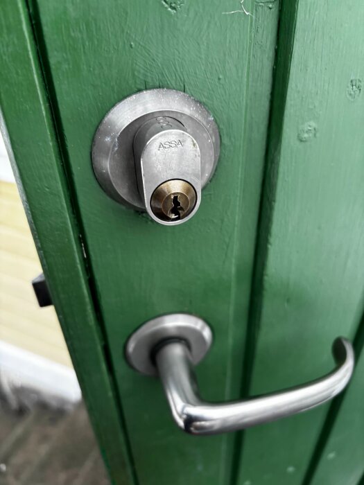 Grönt dörrlås av märket ASSA med dörrhandtag i silverfärg, monterat på en grön dörr.