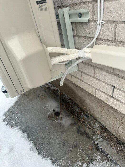 Värmepump frånluftstorkning orsakar vattensamling och isbildning på marken nära husfasaden.