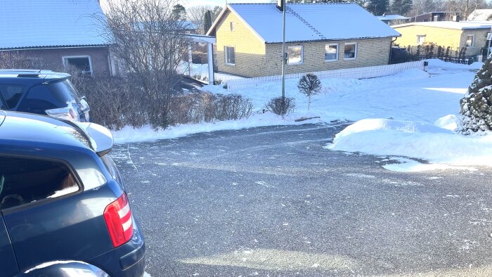 Snötäckt uppfart med bilar och hus i bakgrunden, snön bortblåst från vissa områden.