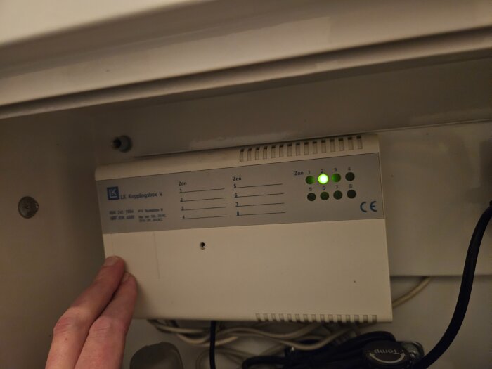 Närbild av en LK kopplingsbox med en grön lampa tänd på zon 1 och en hand som pekar på boxen.