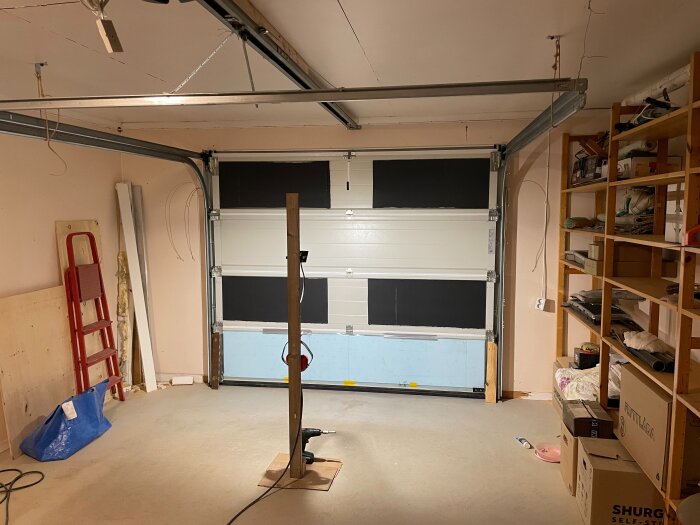 Översiktsbild på ett garage med isolerad garageport och diverse verktyg, material och lådor runtom.