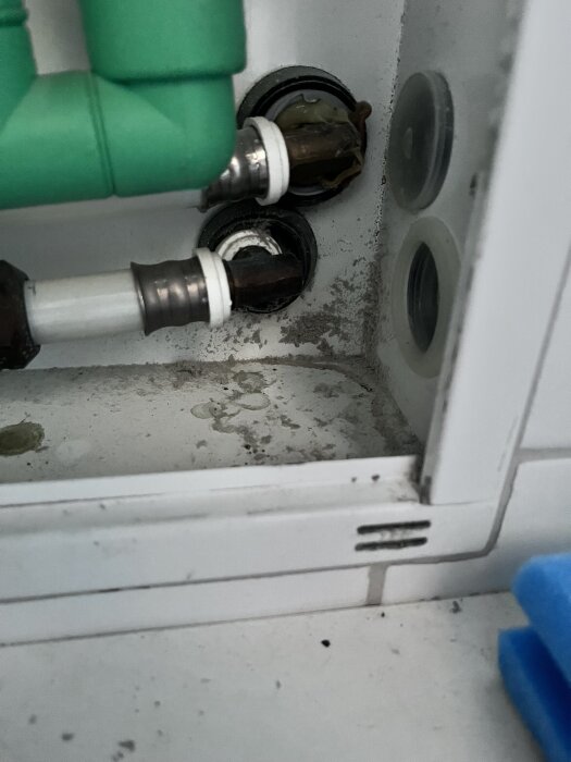 Närbild av rörinstallation med tecken på damm och smuts, synlig tätning kring röranslutningarna i en vit låda.
